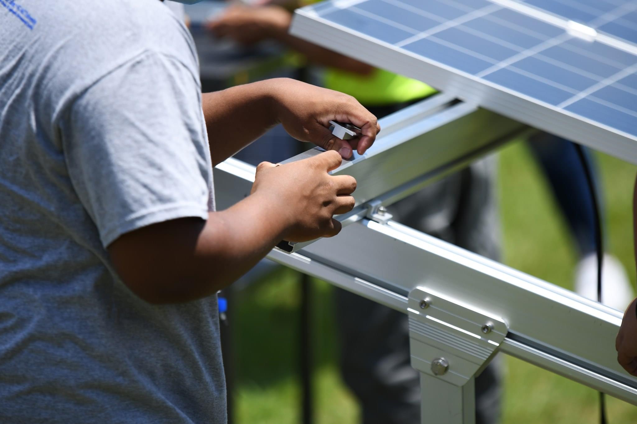 An anonymous person’s torso is shown as they adjust the structure holding up a solar panel.